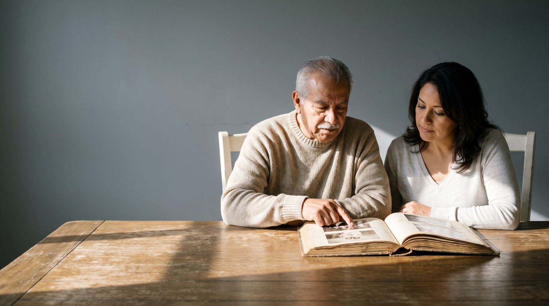 An older man and a woman sitting side by side at a dining table, looking through a photo album together